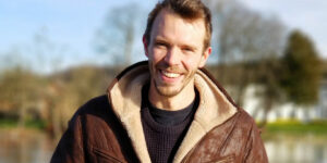 A young male geography graduate, outside, smiling.
