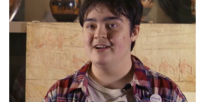 Eadwyn is sitting in the Ure Museum wearing checked shirt and badges