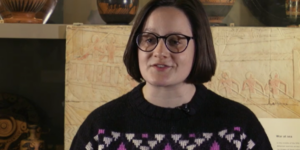 Ela sitting in Ure Museum wearing black , purple and white jumper